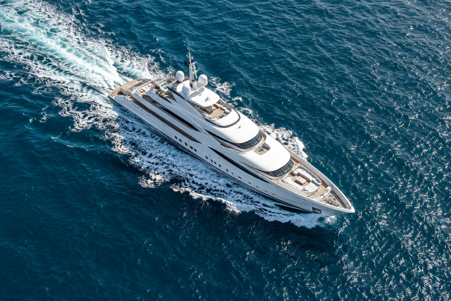 Bird’s-eye view of a white superyacht underway with a foaming wake in the open sea
